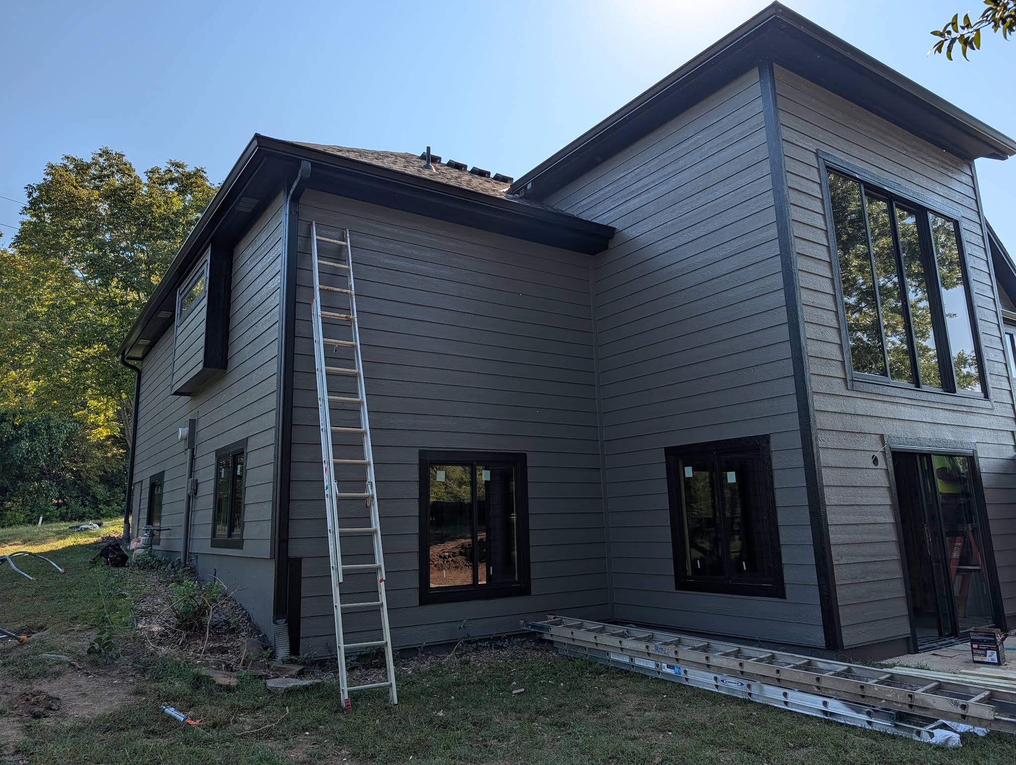 Gutters to Glory work photo showing a two-story home with dark gutters and a ladder beside the roofline.